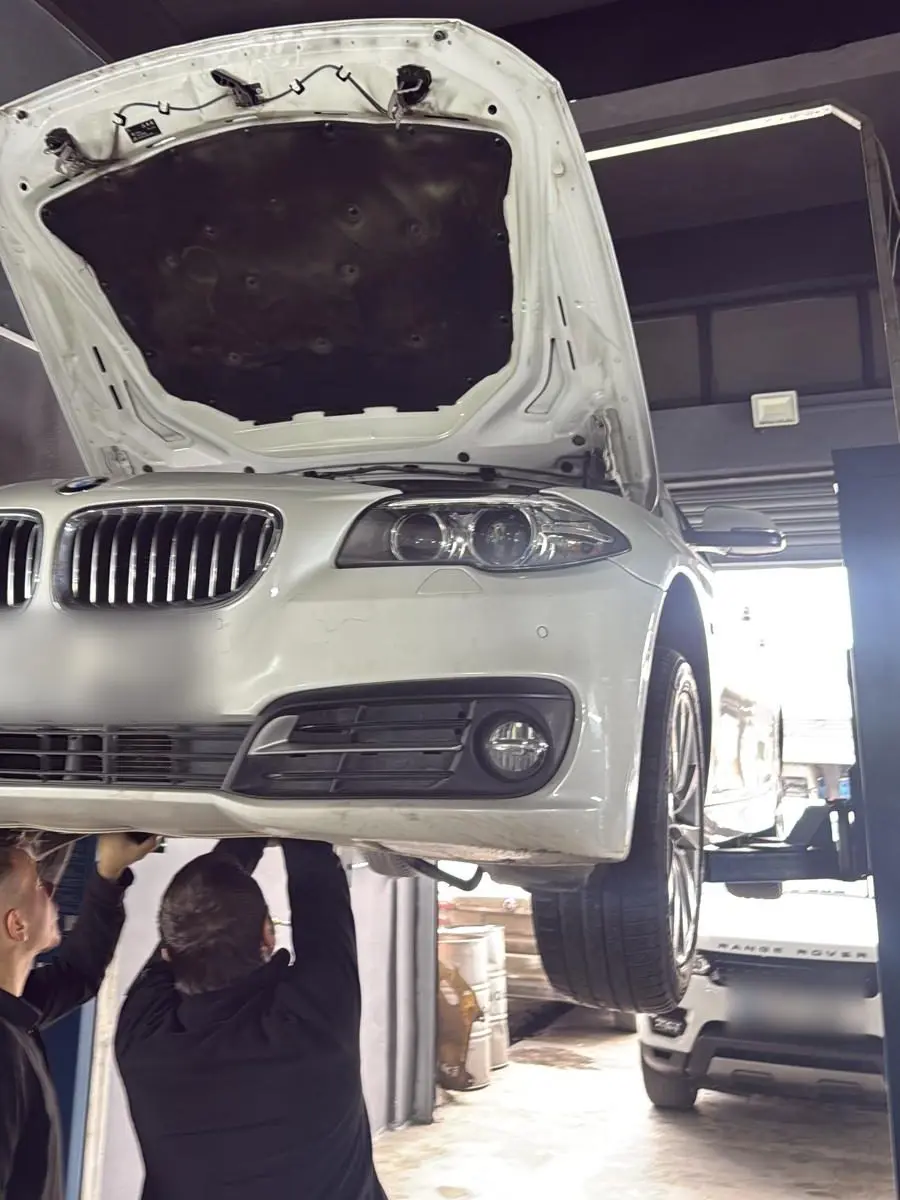 Lift üzerinde kaldırılmış BMW 5 Serisi'nin alt takımını kontrol eden iki teknisyen