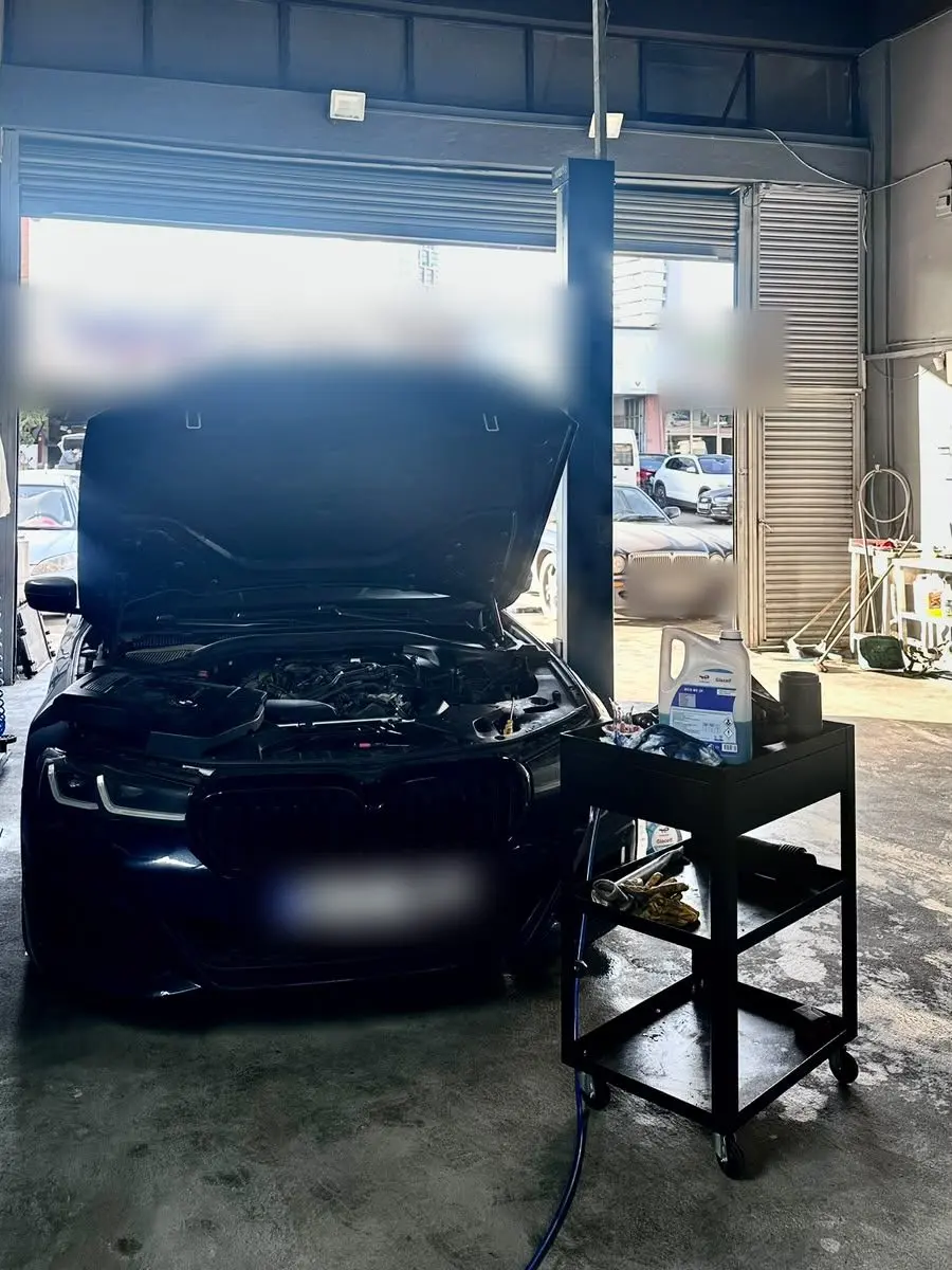 Kaputu açık BMW 5 Serisi ve yanındaki servis arabasında duran bakım sıvıları